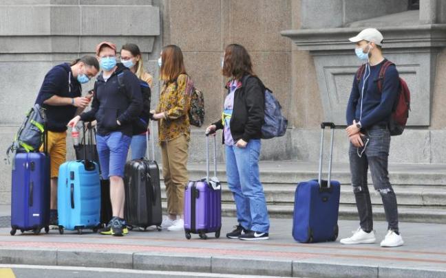 Varios viajeros esperan al autobús con sus maletas y mascarillas.