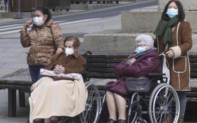 Dos personas ancianas dependientes en silla de ruedas junto a sus cuidadoras.