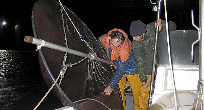 Dos arrantzales vascos pescando angulas desde una embarcación.