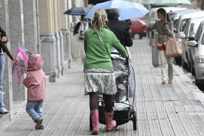 Una mujer pasea con dos niños por una calle.
