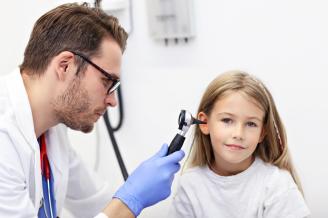 Un médico explora con un otoscopio el oído de una niña.