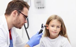 Un médico explora con un otoscopio el oído de una niña.