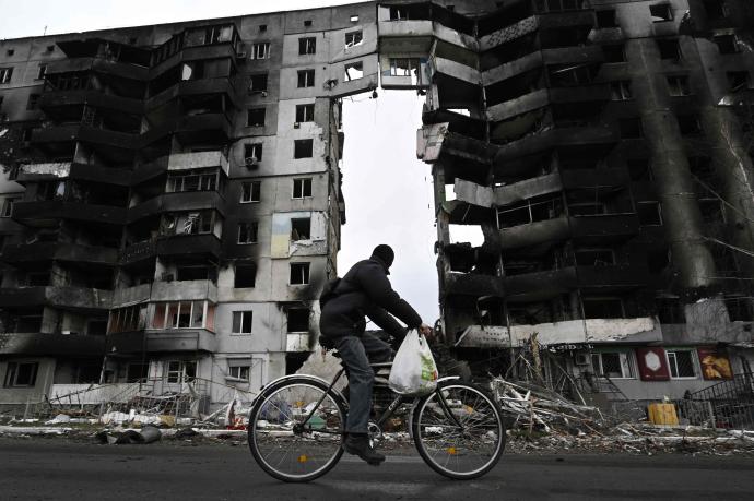 Un hombre pasea en bici junto a un edificio destruido en Borodianka.