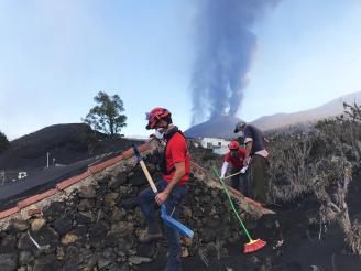 Felipe Murillo y Alain Bravo retiran ceniza de la casa de un palmeño con el volcán de fondo.