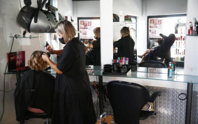 Una peluquera trabajando con mascarilla y medidas de protección debido a la pandemia del coronavirus.