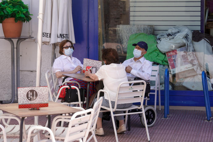 Varias personas con mascarilla conversan sentados en la terraza de un bar.