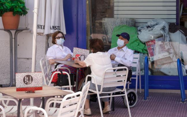 Varias personas con mascarilla conversan sentados en la terraza de un bar. Varias personas con mascarilla conversan sentados en la terraza de un bar.