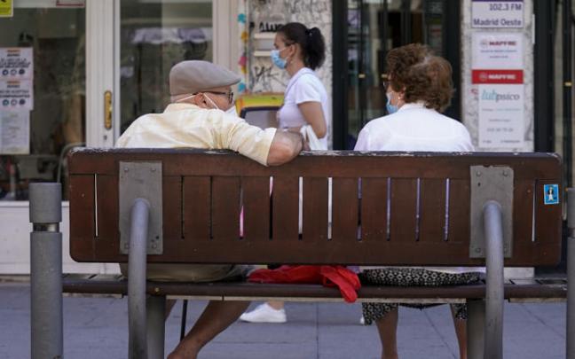 Una pareja de ancianos con mascarilla sentada en un banco. Una pareja de ancianos con mascarilla sentada en un banco.