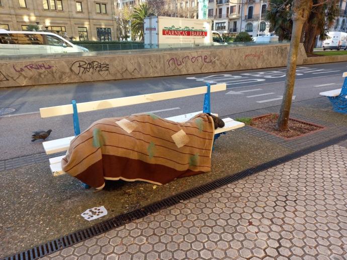 Un hombre duerme en un banco de la calle Reina Regente.