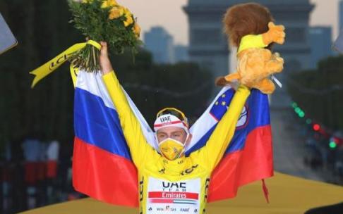 Tadej Pogacar, envuelto en la bandera de Eslovenia en el podio de los Campos Elíseos, celebra la victoria en el Tour. Tadej Pogacar, envuelto en la bandera de Eslovenia en el podio de los Campos Elíseos, celebra la victoria en el Tour.