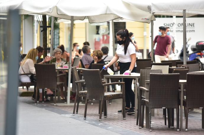 Una camarera desinfectando una mesa de la terraza de un bar