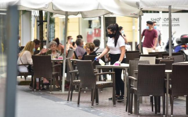 Una camarera desinfectando una mesa de la terraza de un bar