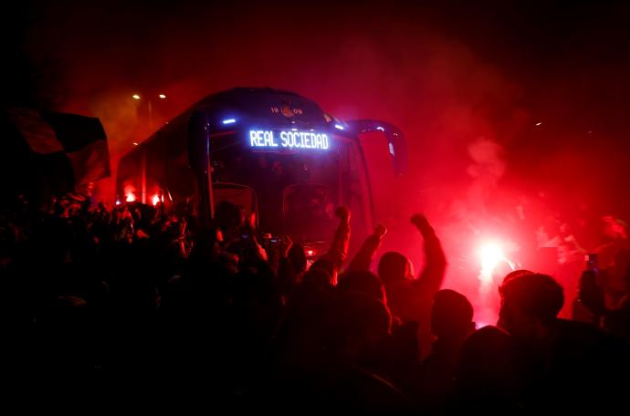 Aficionados de la Real Sociedad reciben con bengalas al autobús de su equipo.