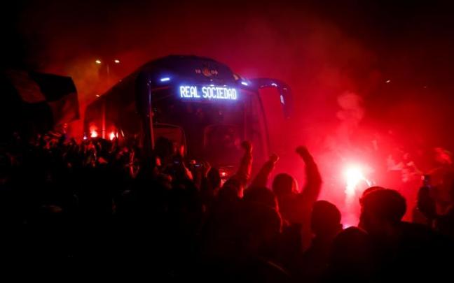 Aficionados de la Real Sociedad reciben con bengalas al autobús de su equipo.