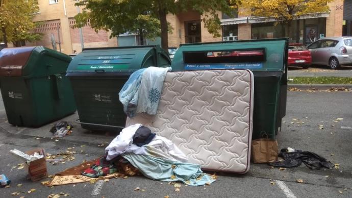 Un colchón junto a basura en un contenedor.