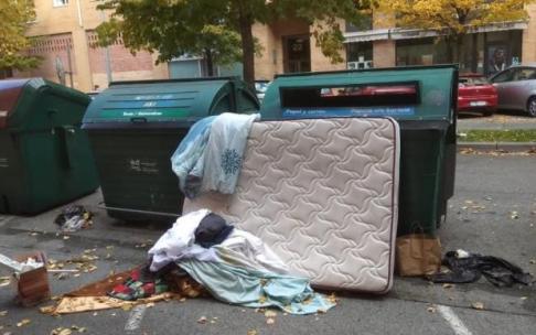 Un colchón junto a basura en un contenedor.