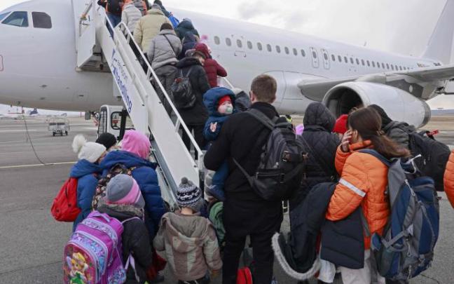 Un grupo de refugiados ucranianos hacen cola para subir a un avión.