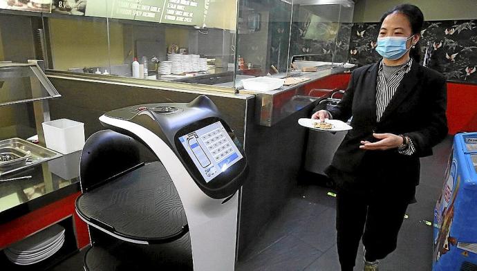 Una trabajadora del restaurante lleva al robot un plato de comida.