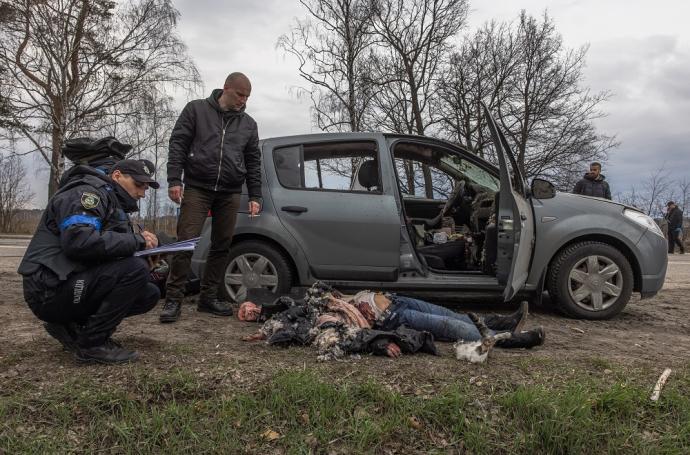 Agentes de policía junto a una mujer que yace en el suelo tras ser asesinada junto a un automóvil, en Bucha.