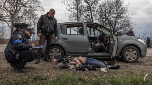 Agentes de policía junto a una mujer que yace en el suelo tras ser asesinada junto a un automóvil, en Bucha.
