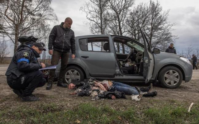 Agentes de policía junto a una mujer que yace en el suelo tras ser asesinada junto a un automóvil, en Bucha.
