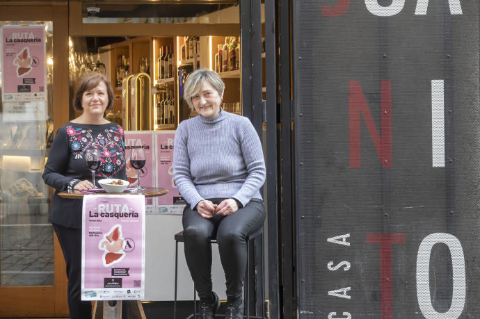 Beatriz Huarte, secretaria general de ANAPEH y Mª Ángeles Elizalde de Casa Juanito en la calle Estafeta con el cartel anunciador de la Ruta de la Casquería