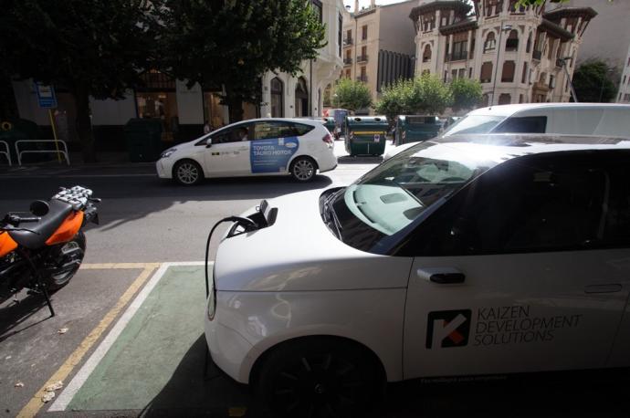 Un taxi circula por la avenida San Ignacio de Pamplona, junto a un punto de recarga de vehículos eléctricos.