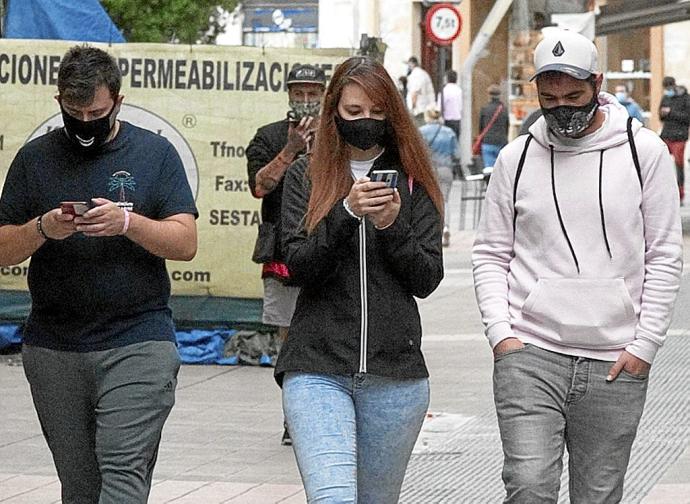 Varios jóvenes caminando por la calle con mascarilla mirando sus teléfonos móviles mientras andan. Foto: Josu Chavarri