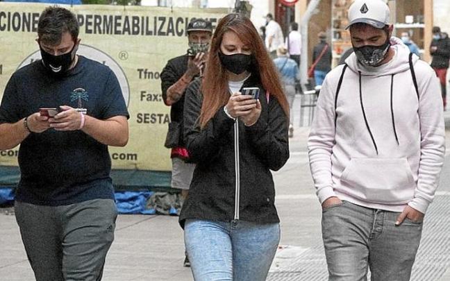 Varios jóvenes caminando por la calle con mascarilla mirando sus teléfonos móviles mientras andan. Foto: Josu Chavarri Varios jóvenes caminando por la calle con mascarilla mirando sus teléfonos móviles mientras andan. Foto: Josu Chavarri