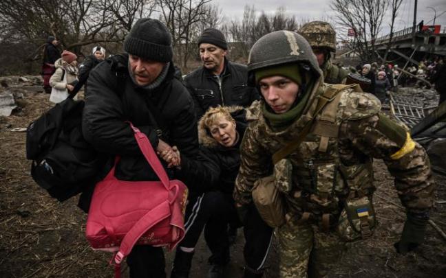 Una mujer recibe ayuda mientras la gente cruza un puente destruido en la ciudad de Irpin.