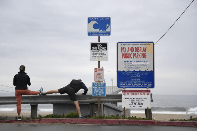 Dos personas hacen deportes junto a un cartel que alerta del peligro de tsunami en California.