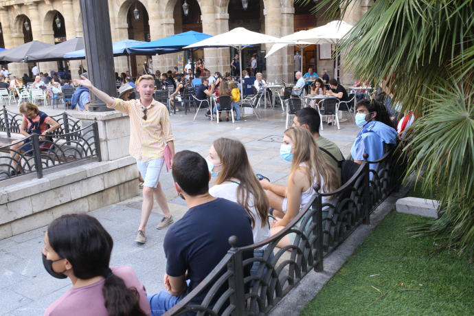 Un guía da explicaciones a varios turistas en una Plaza Nueva con las terrazas abarrotadas.