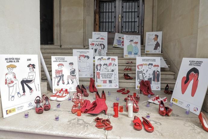 Varios pares de zapato de color rojo, velas y carteles contra la violencia contra las mujeres a las puertas de la Subdelegación del Gobierno en Alicante