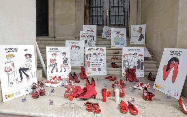 Varios pares de zapato de color rojo, velas y carteles contra la violencia contra las mujeres a las puertas de la Subdelegación del Gobierno en Alicante