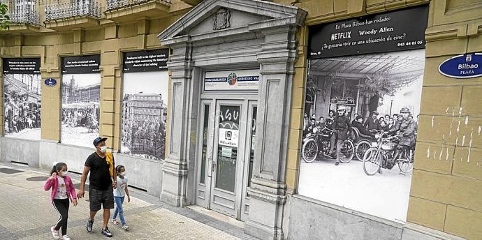 Un padre y sus hijas pasan delante de las imágenes de la Belle Époque colocadas en la plaza de Bilbao.