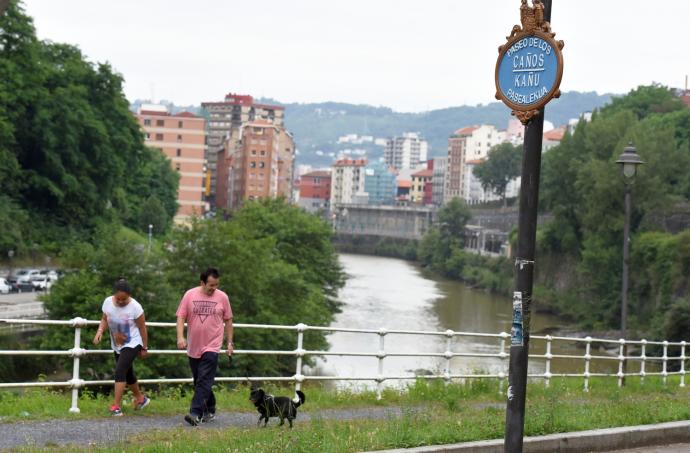 Una pareja pasea a su perro por el paseo de los Caños del barrio bilbaino de Atxuri.