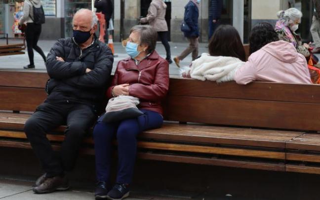 Varias personas descansan en un banco del centro de Vitoria.