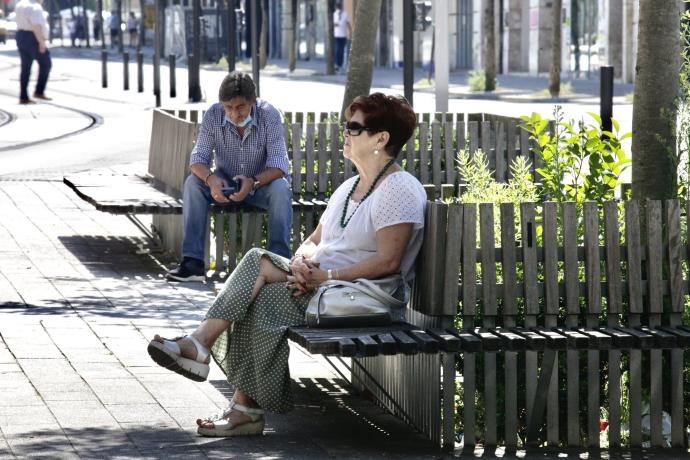 Dos personas descansan en unos bancos en Vitoria.