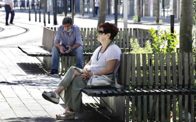 Dos personas descansan en unos bancos en Vitoria.