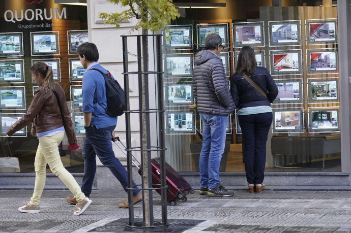 Dos personas miran el escaparate de una inmobiliaria.