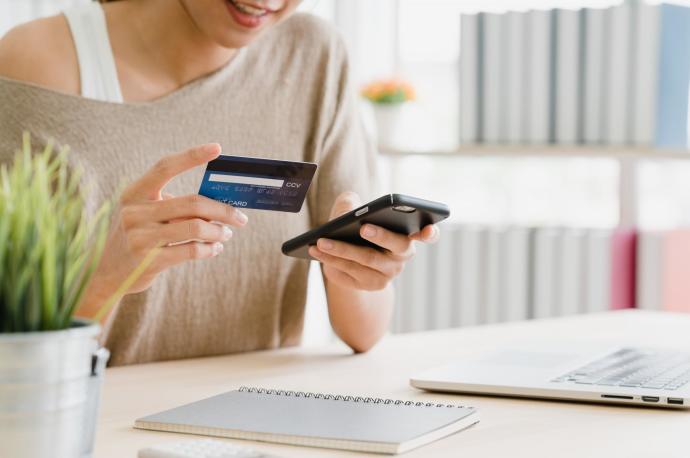 Una mujer se dispone ha realizar una compra a través de su móvil usando una tarjeta de crédito.