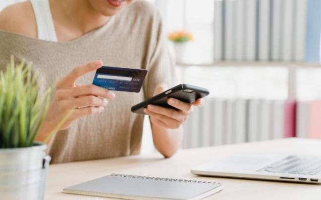 Una mujer se dispone ha realizar una compra a través de su móvil usando una tarjeta de crédito. Una mujer se dispone ha realizar una compra a través de su móvil usando una tarjeta de crédito.