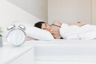 Una mujer duerme con un despertador en la mesilla.