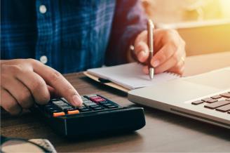 Un hombre hace cuentas con una calculadora junto a su ordenador.