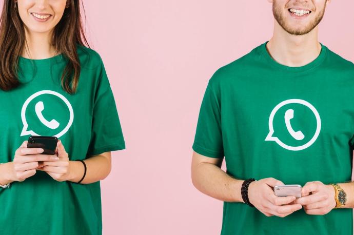 Dos jóvenes con camisetas con el logotipo de WhatsApp y sendos móviles.