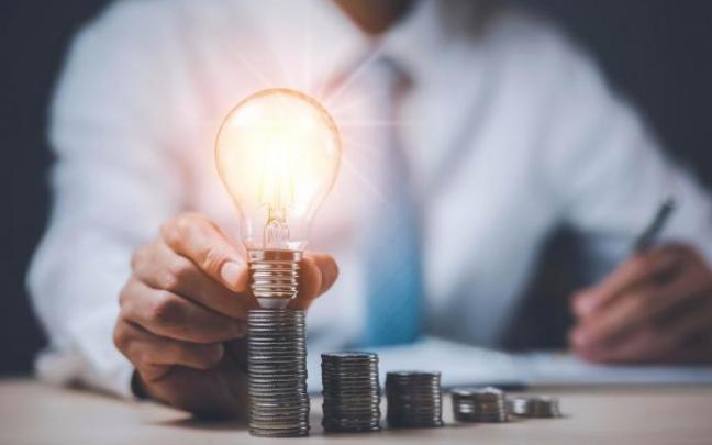 Recreación de una bombilla encendida sobe una de columna de monedas.