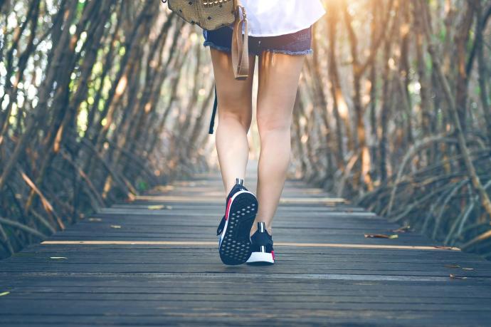 Una mujer con deportivas camina sobre un puente de madera.