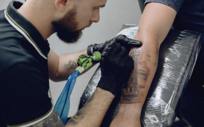 Un tatuador realiza un tatuaje en el brazo de un hombre. Un tatuador realiza un tatuaje en el brazo de un hombre.