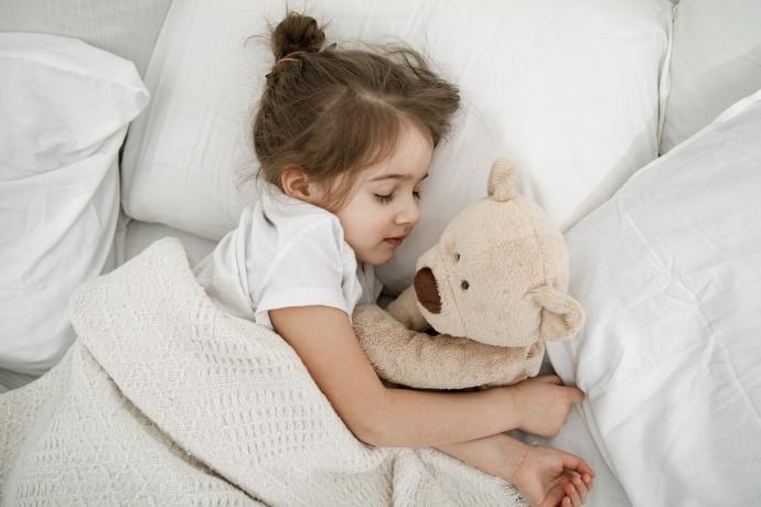 Una niña acostada en la cama con un osito de peluche.