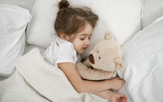 Una niña acostada en la cama con un osito de peluche.